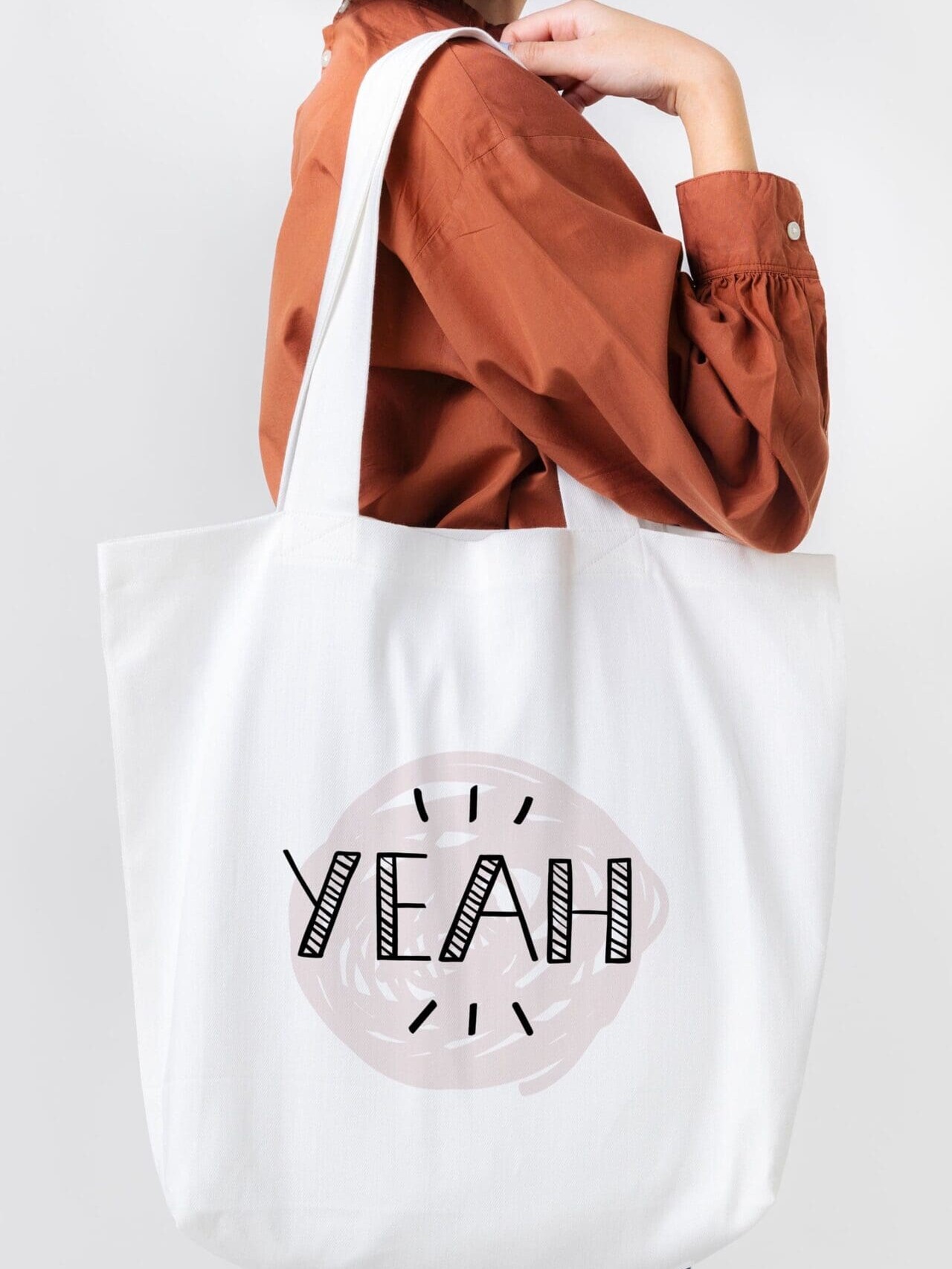 Personne portant un grand sac fourre-tout blanc sur lequel est imprimé « YEAH » en lettres noires et grasses. L'individu porte une chemise à manches longues orange.