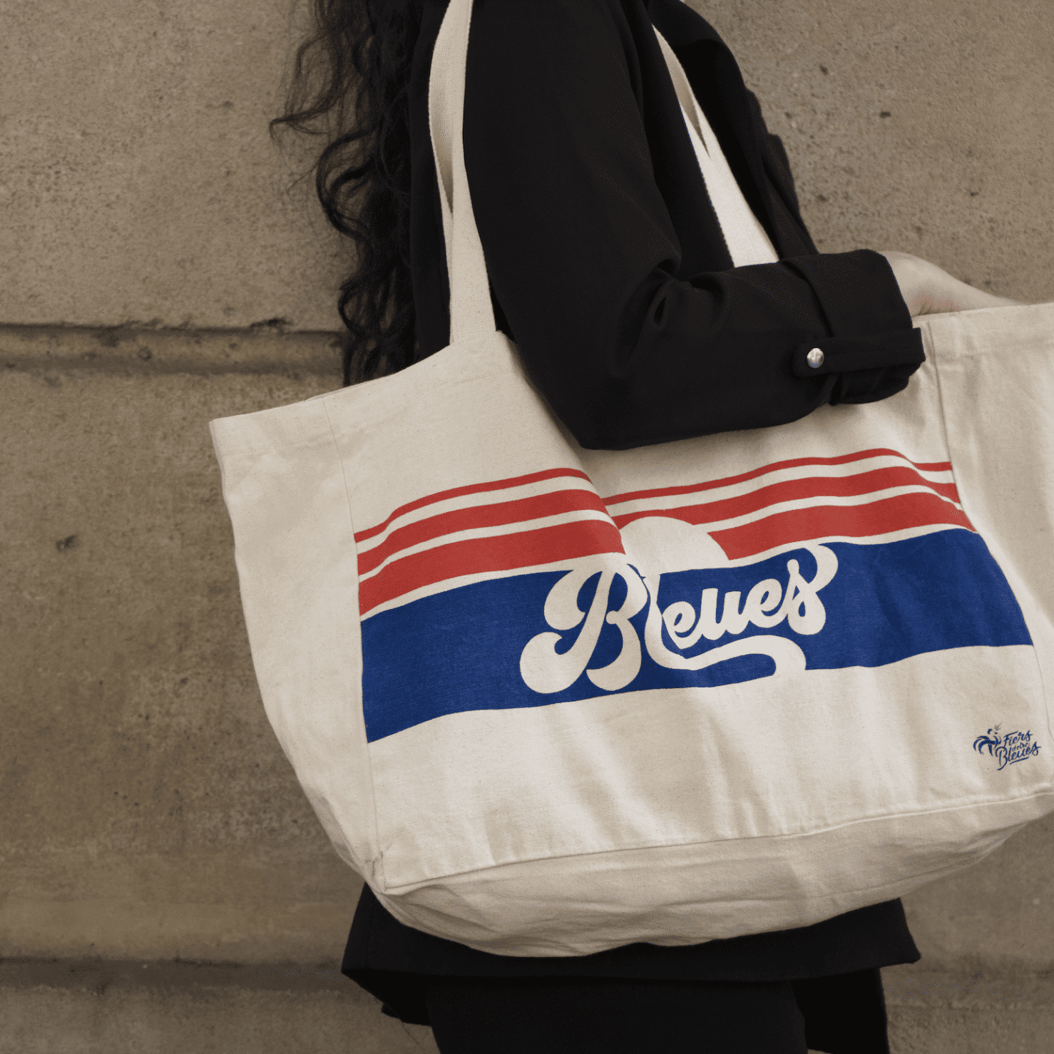 Personne portant un sac fourre-tout beige à rayures rouges et bleues et le mot « Reves » imprimé dessus.