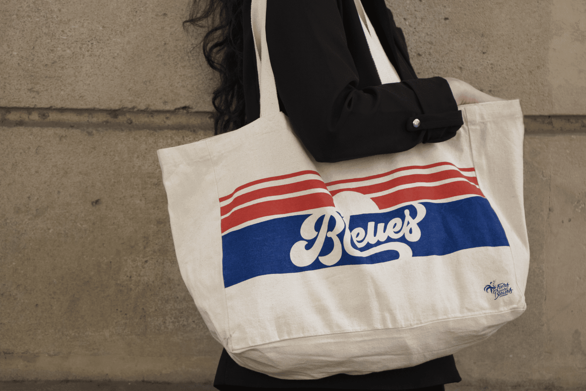 Personne portant un sac fourre-tout beige à rayures rouges et bleues et le mot « Reves » imprimé dessus.