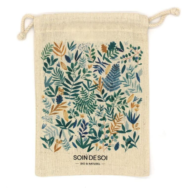 Un sac à cordon beige avec le texte « SOIN DE SOI BIO & NATUREL » en bas, présentant un motif coloré de diverses feuilles et feuillages dans des teintes vertes, bleues et orange.