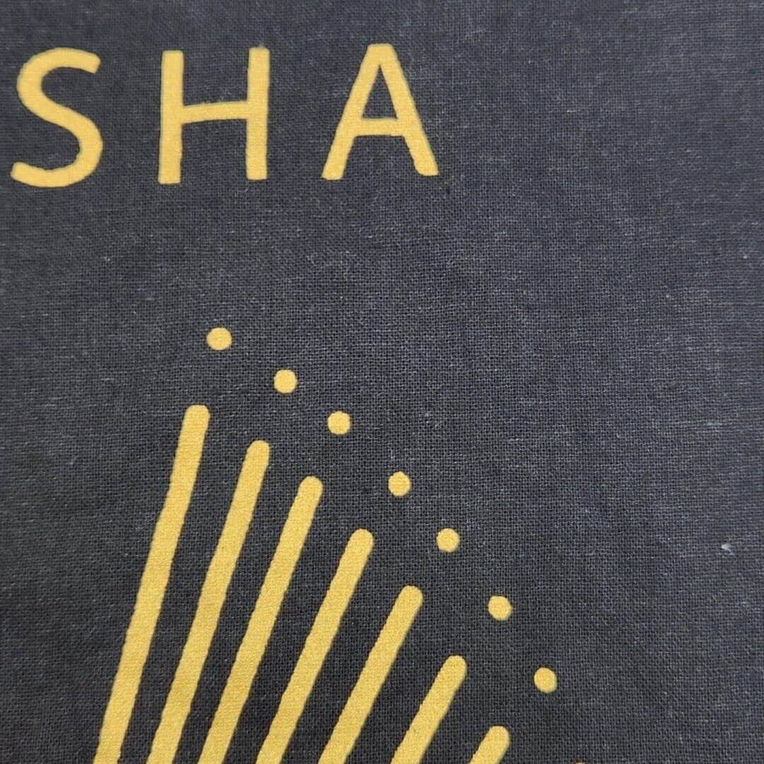 Gros plan d'un tissu foncé avec un motif jaune partiellement visible et les lettres « SHA » imprimées en jaune.