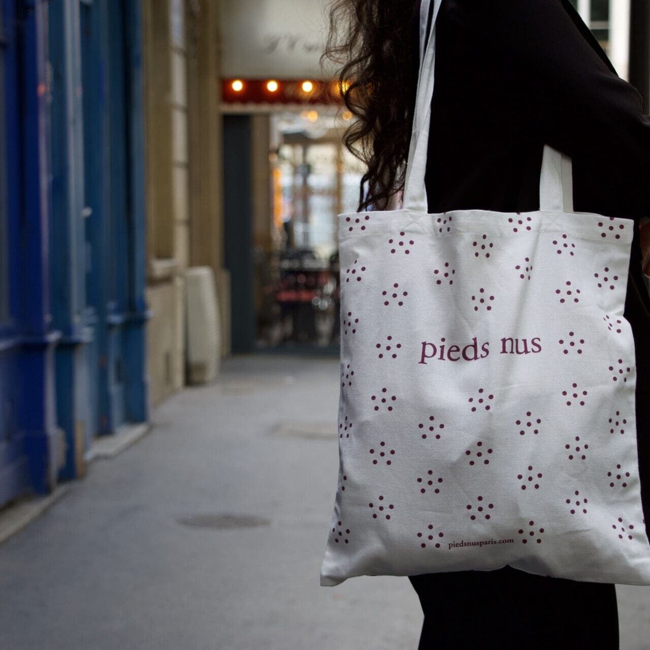 Une personne tient un sac fourre-tout blanc avec un motif de petites fleurs et le texte « pieds nus » alors qu'elle marche dans une rue de la ville.